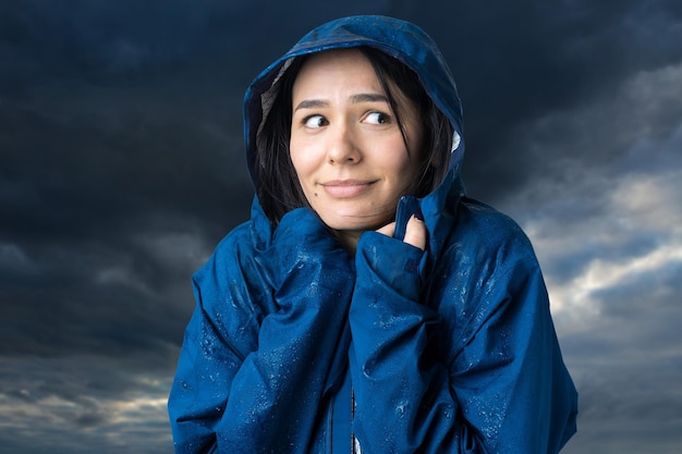 Retrato de uma menina sorridente, vestida com uma capa de chuva azul e pingentes posando com capuz