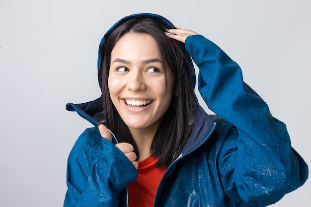 Retrato de uma menina sorridente, vestida com uma capa de chuva azul em gotas, posando com capuz sobre fundo cinza