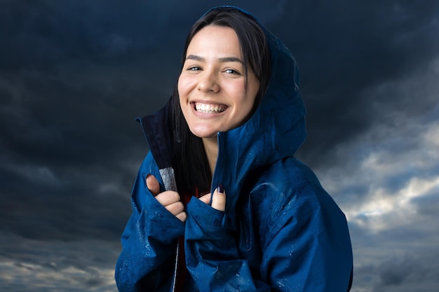 Retrato de uma menina sorridente, vestida com uma capa de chuva azul em gotas, posando com capuz sobre fundo cinza