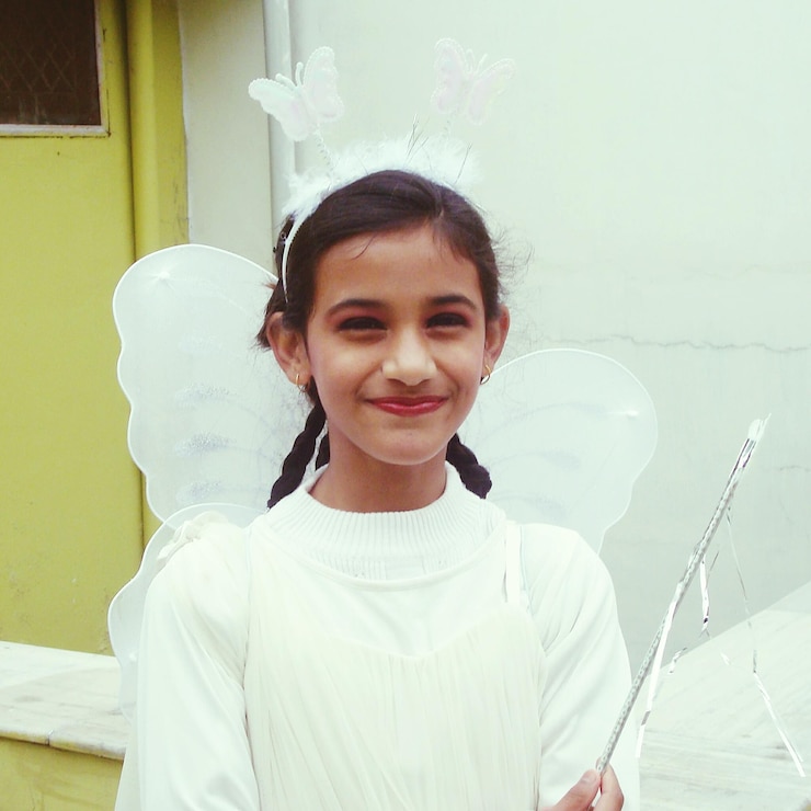 Foto retrato de uma menina sorridente vestindo um traje de anjo contra a parede