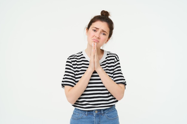 Foto retrato de uma menina triste implorando ajuda de pé em postura de súplica com fundo branco