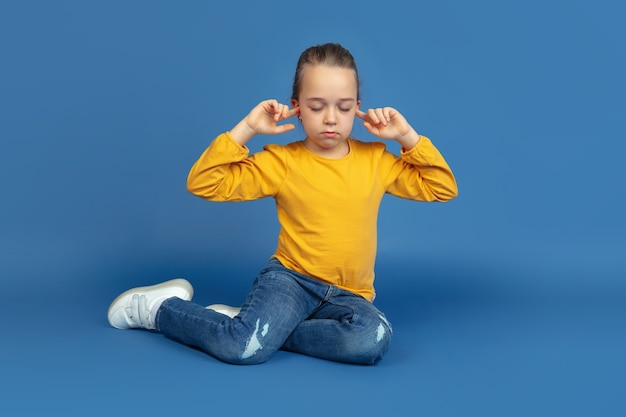 Retrato de uma menina triste sentada isolada no fundo azul do estúdio. como é ser autista. problemas modernos, nova visão das questões sociais. conceito de autismo, infância, saúde, medicina.