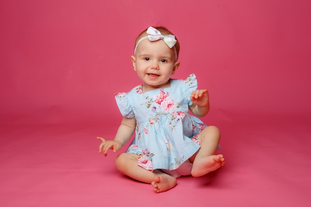 Foto retrato de uma menina vestida com um vestido sentada em um fundo rosa