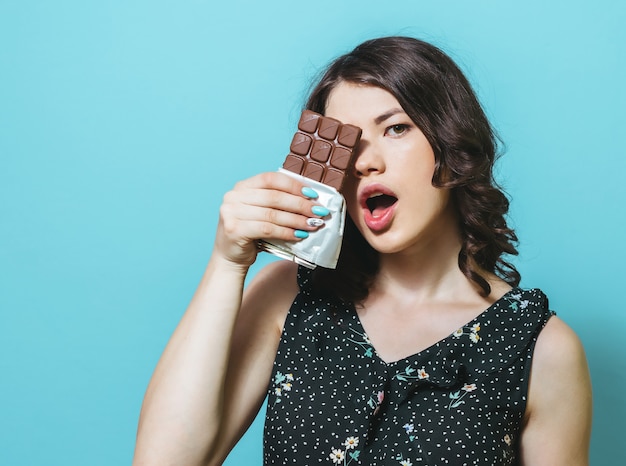 Retrato de uma moça chocada isolada sobre a parede azul, guardando o chocolate.