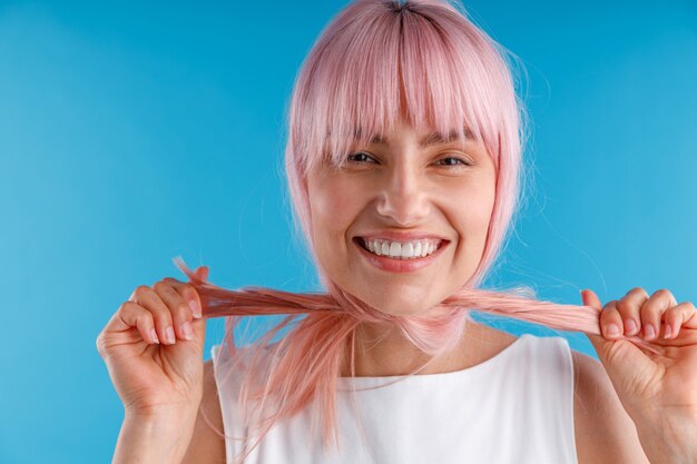 Retrato de uma modelo feminina alegre brincando com cabelo liso rosa e liso enrolado no pescoço