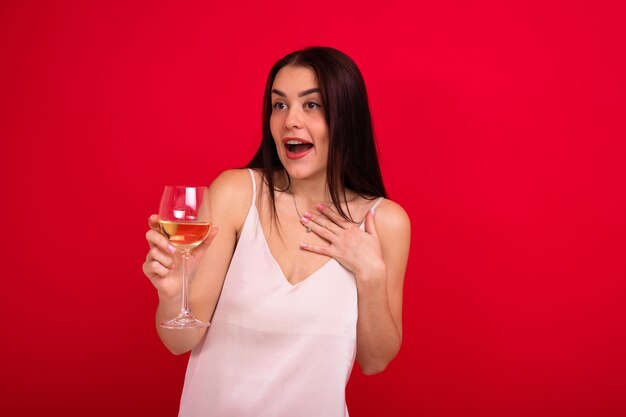 Retrato de uma morena em um vestido branco com um copo de vinho em um fundo vermelho