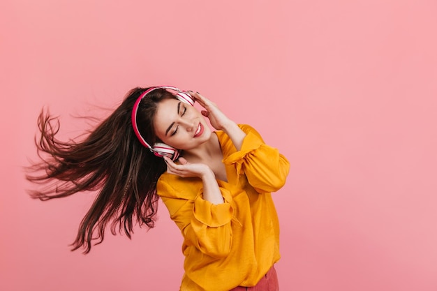 Retrato de uma morena positiva tocando cabelo enquanto dançava garota com roupas estilosas curtindo a melodia