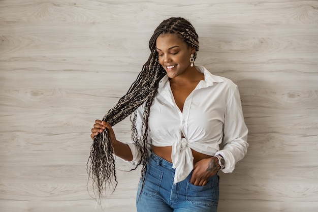 Foto retrato de uma mulher adulta afro-americana alegre segurando seus longos cabelos. mulher adulta com tranças pretas e amarelas, posando em um fundo de parede e olhando para baixo.