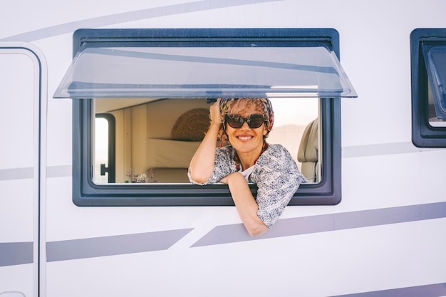 Retrato de uma mulher adulta alegre olhando para fora de uma janela de van campista e aproveitando o estilo de vida de viagem Pessoas do sexo feminino sorriem e procuram uma foto Férias de verão turista de viagem