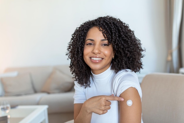 Foto retrato de uma mulher africana feliz vacinada mostrando seu braço após a injeção da vacina antiviral contra o coronavírus conceito da campanha de imunização contra a covid-19