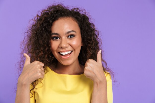 Retrato de uma mulher afro-americana animada em roupas casuais, sorrindo com o polegar para cima isolado na parede violeta