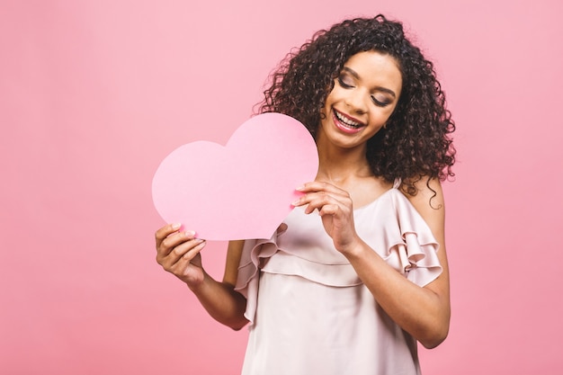 Retrato de uma mulher afro-americana atraente e sorridente, isolada contra um fundo rosa com um grande coração rosa