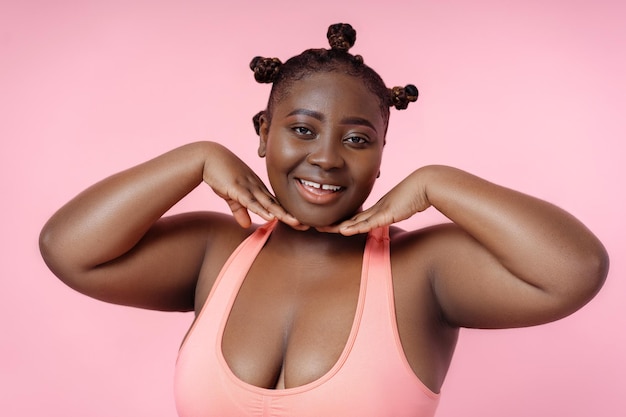 Retrato de uma mulher afro-americana com corpo positivo em top rosa posando para a foto tocando o rosto isolado em fundo rosa conceito de estilo de vida saudável cuidados com a pele