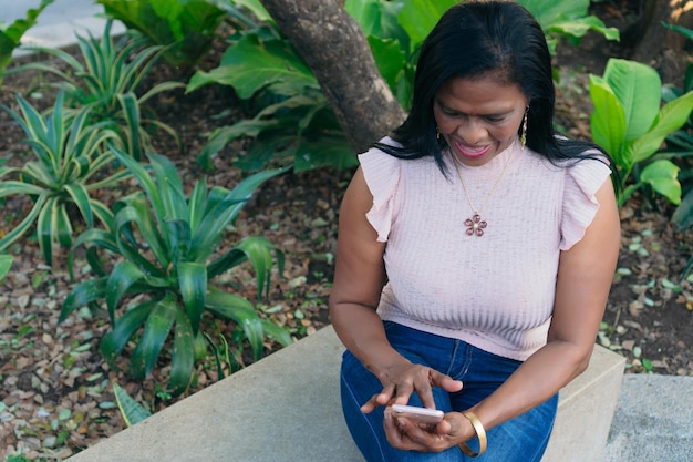 Retrato de uma mulher afro-americana de meia idade checando o celular no parque