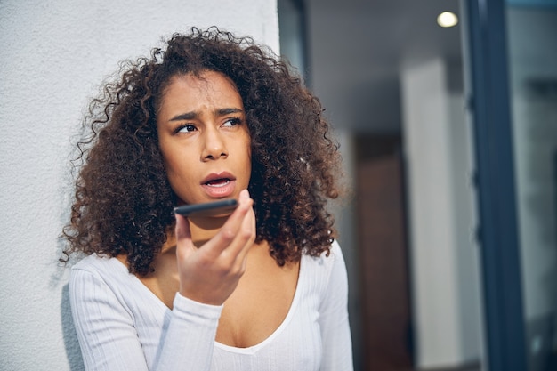 Retrato de uma mulher afro-americana encostada na parede enquanto fala ao celular