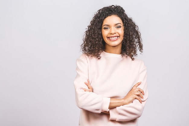 Retrato de uma mulher afro-americana positiva bonita que está com os braços cruzados isolados contra um fundo branco.