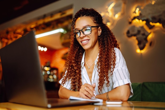 Retrato de uma mulher afro-americana sentada no café fazendo uma chamada de vídeo no computador portátil