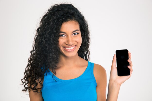 Retrato de uma mulher afro-americana sorridente, mostrando a tela do smartphone em branco, isolada em uma parede branca.