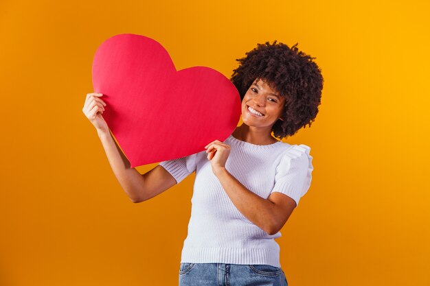 Retrato de uma mulher afro sorridente segurando um cartão com um grande coração vermelho