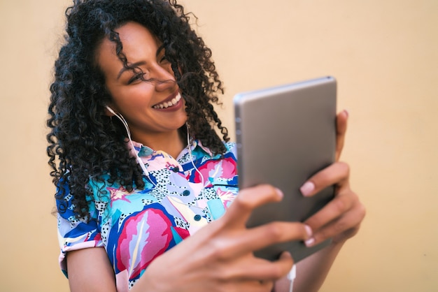Retrato de uma mulher afro, tirando selfies com seu tablet digital contra a parede amarela. Conceito de tecnologia.