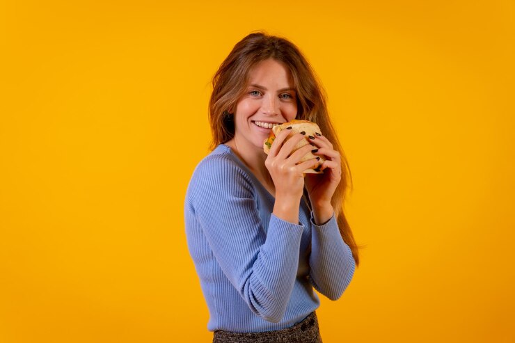 Foto retrato de uma mulher alegre comendo um sanduíche em um fundo amarelo comida saudável e vegetariana