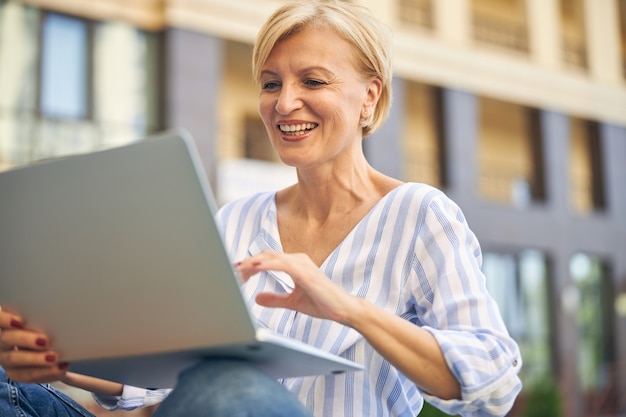 Retrato de uma mulher alegre e agradável com um corte de cabelo curto trabalhando em seu laptop ao ar livre