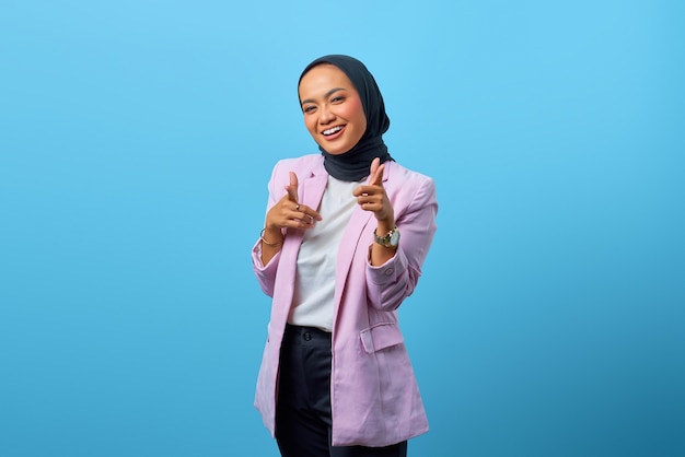 Retrato de uma mulher asiática alegre apontando o dedo para a câmera sobre fundo azul