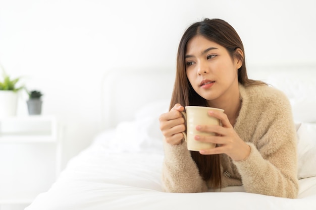 Retrato de uma mulher asiática bonita sorridente, feliz e alegre, relaxando bebendo e olhando para a xícara de café quente ou chá.