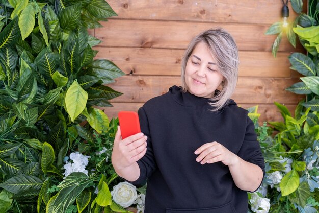 Retrato de uma mulher asiática de meia idade sorridente segurando um smartphone nas mãos em um fundo de prancha de madeira