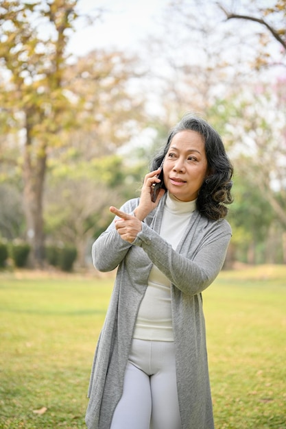 Retrato de uma mulher asiática feliz de 60 anos falando ao telefone enquanto caminhava no parque