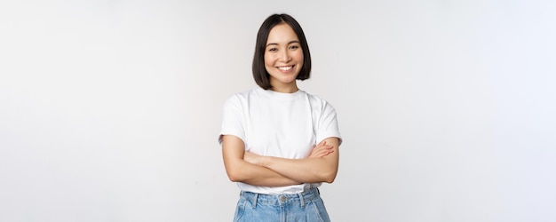 Retrato de uma mulher asiática feliz sorrindo posando confiantes braços cruzados no peito em pé contra o fundo do estúdio