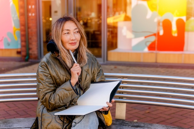 Retrato de uma mulher asiática mais velha feliz escrevendo em um caderno do lado de fora