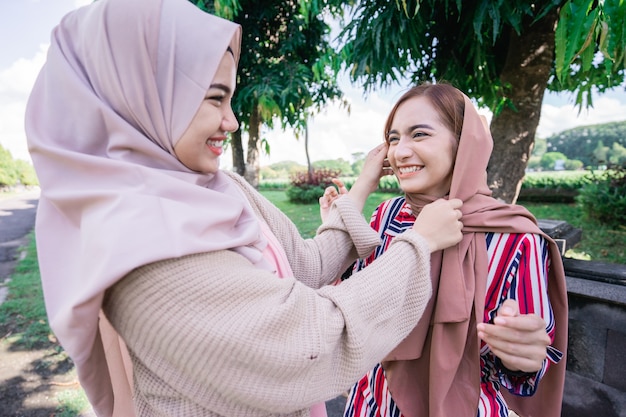 Retrato de uma mulher asiática muçulmana feliz consertando um amigo hijab durante uma reunião ao ar livre