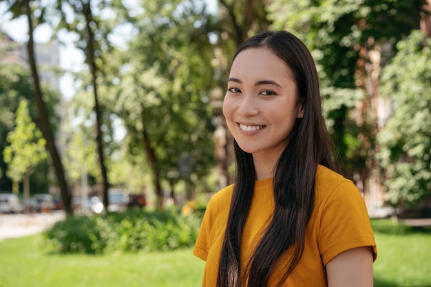 Retrato de uma mulher asiática sorridente, olhando para a câmera em pé no parque