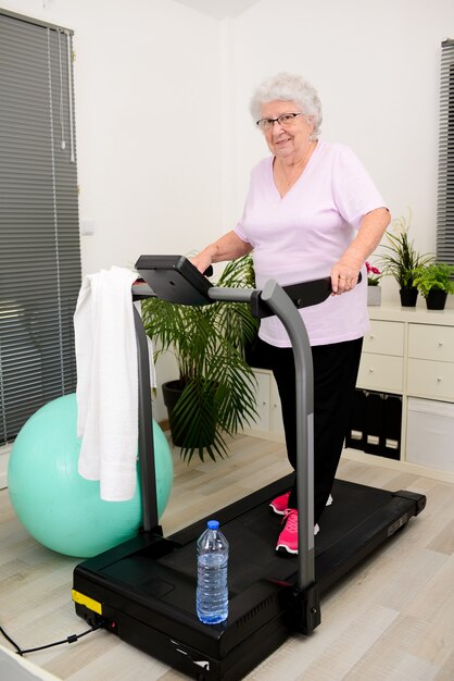 Retrato de uma mulher ativa e dinâmica sênior fazendo esporte fitness em casa caminhando na esteira