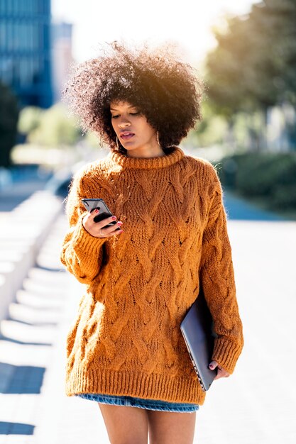 Retrato de uma mulher atraente afro usando telefone celular na rua. Conceito de mulher de negócios