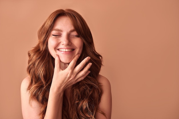 Retrato de uma mulher atraente com cabelo vermelho tocando o queixo com os olhos fechados O sorriso e a beleza de uma mulher