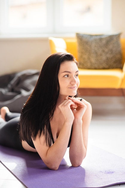 Retrato de uma mulher atraente com cabelos longos escuros relaxando no tapete de ioga depois do treino Jovem saudável em roupas esportivas