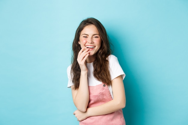 Retrato de uma mulher atraente feliz rindo e se divertindo, sorrindo com os dentes brancos, curtindo o filme engraçado, em pé sobre um fundo azul.