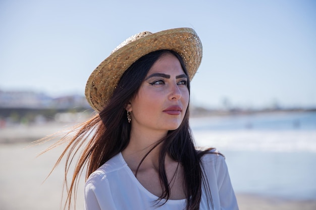 Retrato de uma mulher atraente na praia usando um chapéu de verão e olhando para o lado
