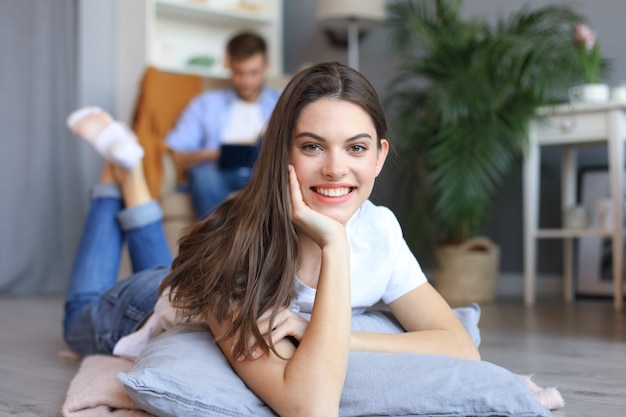 Retrato de uma mulher atraente relaxante no chão com o homem borrado no fundo.