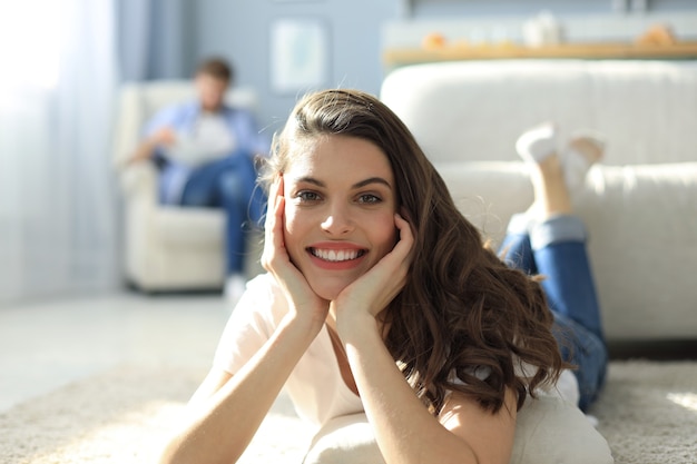 Retrato de uma mulher atraente relaxante no chão com o homem borrado no fundo.