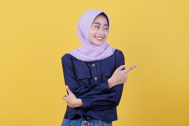 Retrato de uma mulher bonita apontando para cima em um pano casual, usando um hijab em fundo amarelo isolado