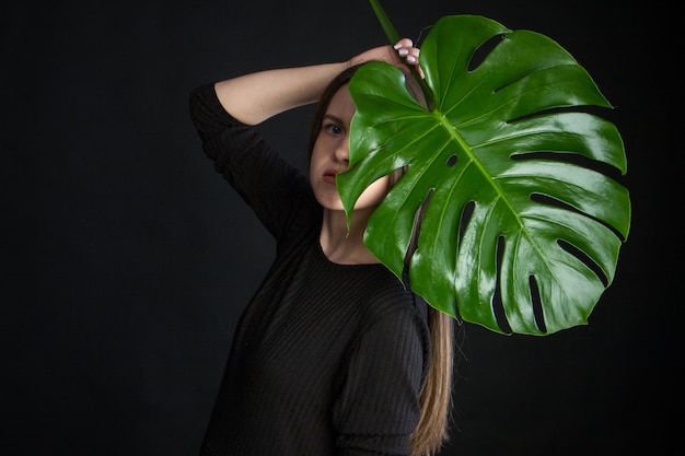 Retrato de uma mulher bonita com folhas tropicais verdes sobre fundo preto