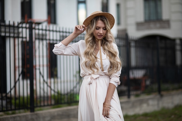 Retrato de uma mulher bonita com longos cabelos loiros em vestido longo branco sai e olha para baixo