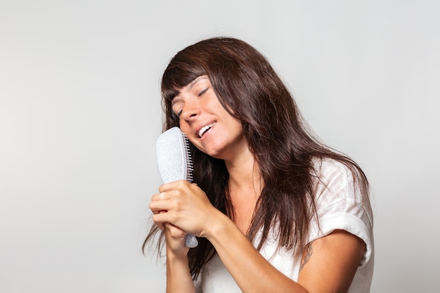 Retrato de uma mulher bonita com tatuagens, cantando em uma escova de cabelo como se fosse um microfone, fechando os olhos. fundo branco. o conceito de cuidado com o cabelo e diversão.