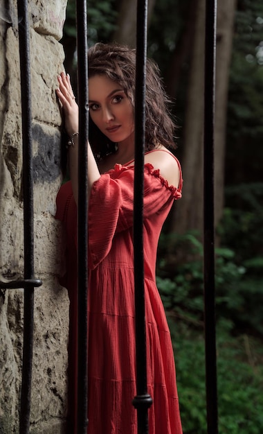 Retrato de uma mulher bonita de vestido vermelho atrás das grades, olhando para a câmera