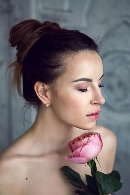 Retrato de uma mulher bonita e atraente em uma toalha cinzenta no banheiro segurando uma rosa vermelha