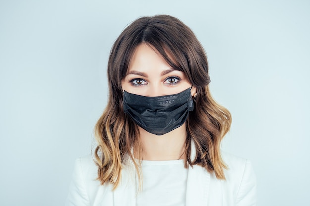 Retrato de uma mulher bonita e jovem médica em um vestido branco médico e máscara preta no rosto em um fundo branco