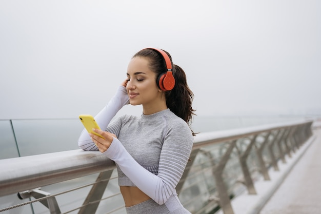 Retrato de uma mulher bonita em roupas esportivas elegantes ouvindo música em fones de ouvido